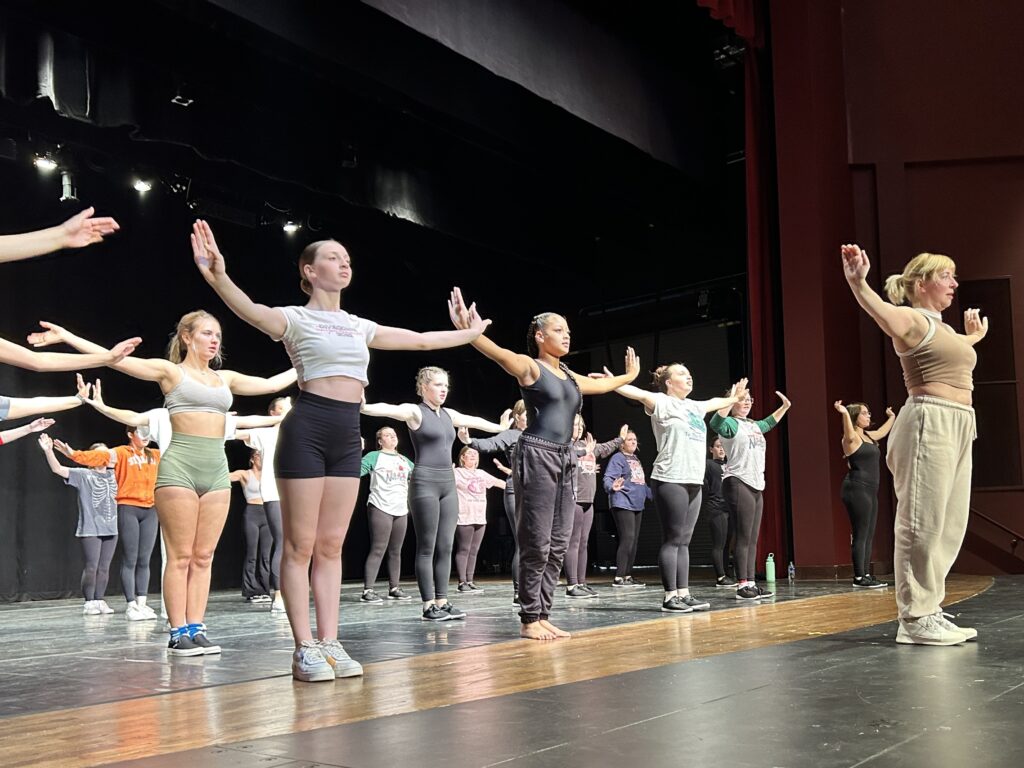 dance students form rows behind an instructor with arms outstretched during a day of dance
