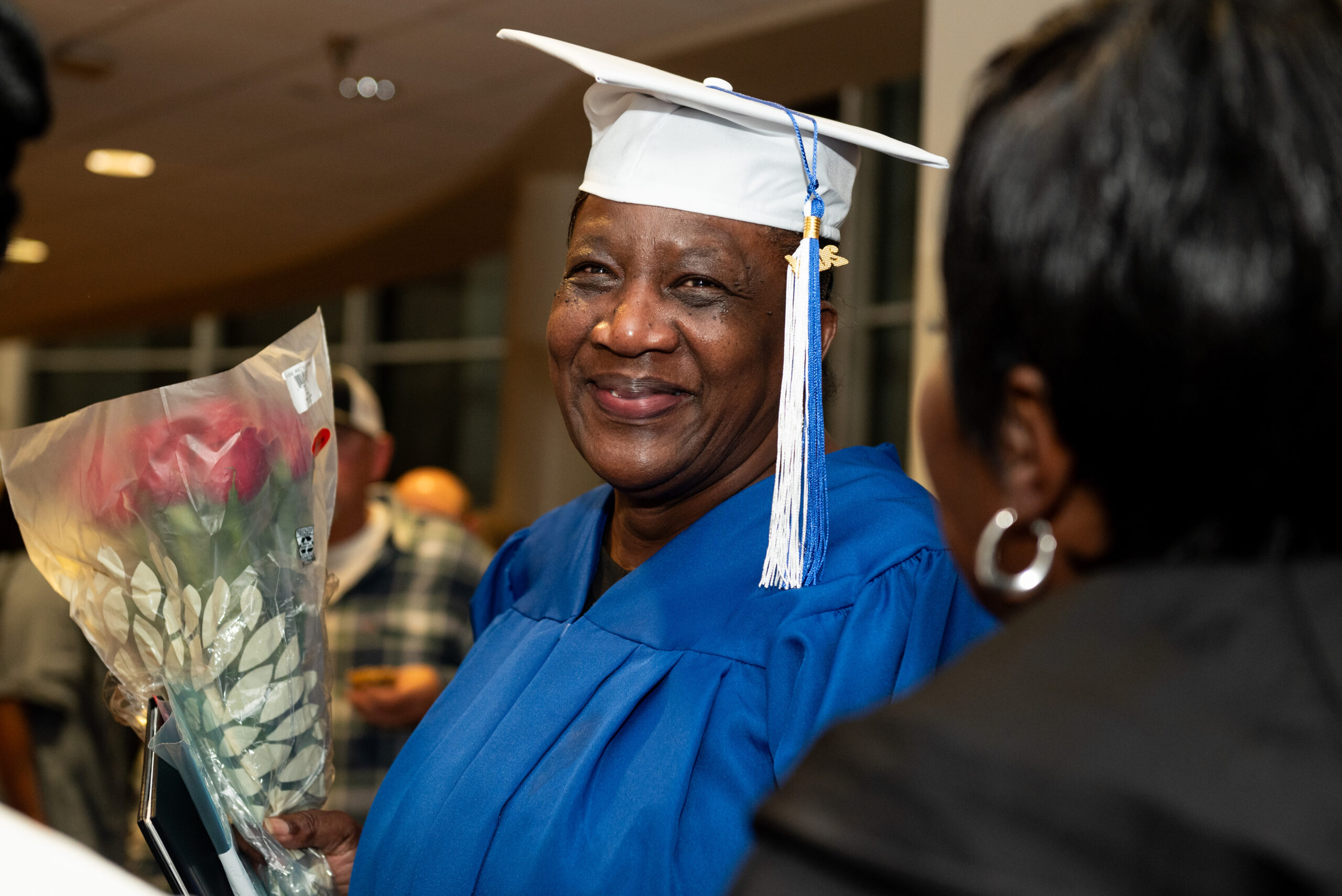 AEG_10-15-24_83 Smiling Adult Education graduate in regalia with a flower bouquet