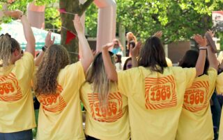 Seven students lined up display the back of their Chesapeake College 60th Anniversary yellow t-shirts received during Spring Fest 2025