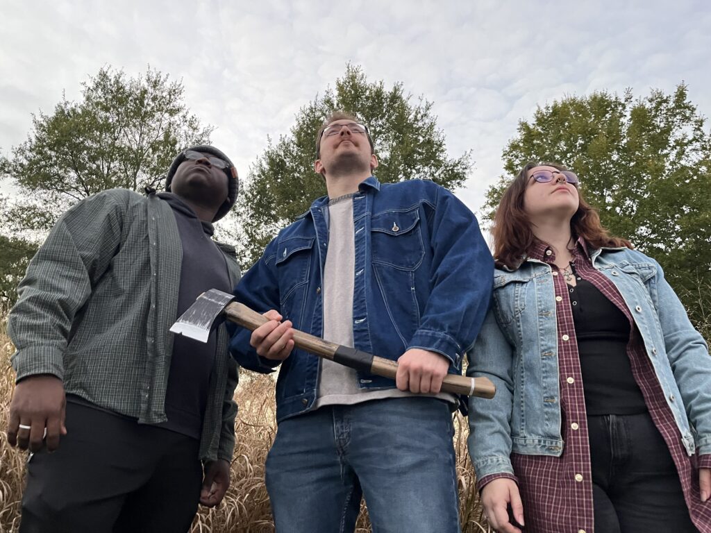 three actors, one holding an ax, set the spooky stage for True Crime Thursday